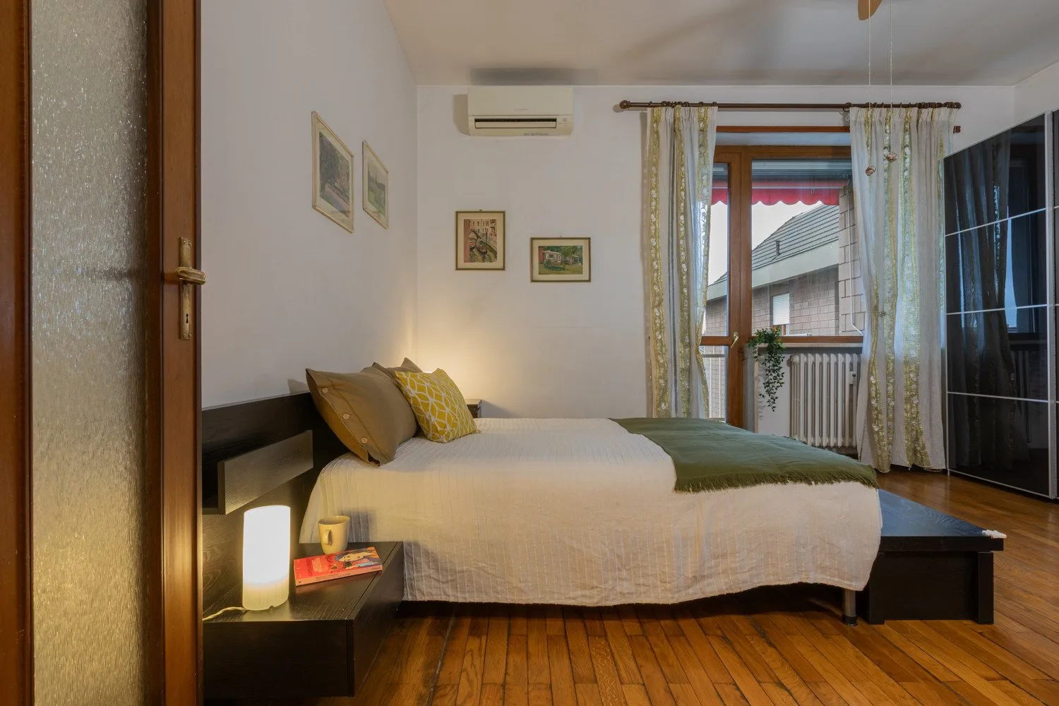 A bedroom with a neatly made bed, framed pictures, and a window with curtains.