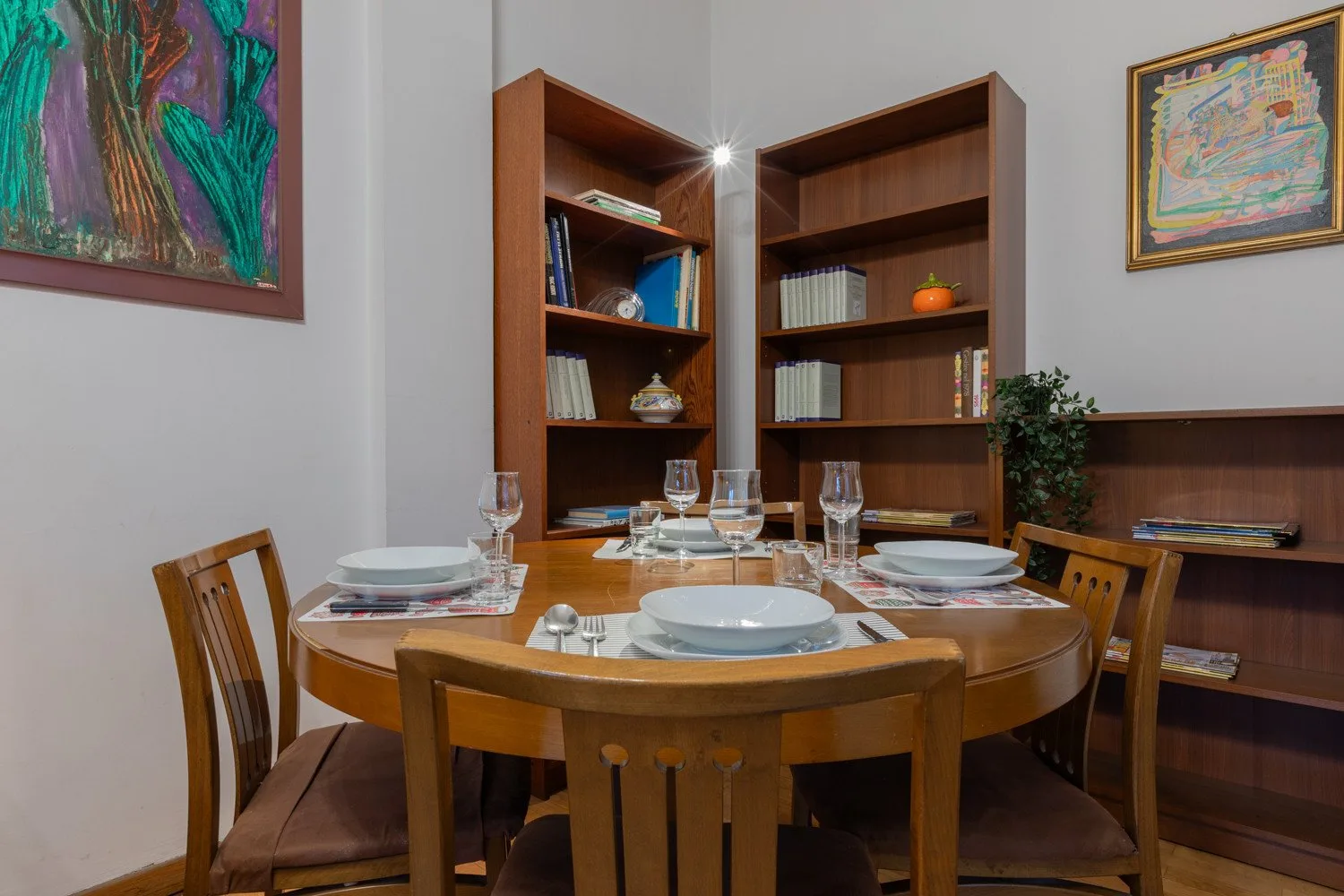 A dining area with a round table set with plates and surrounded by wooden seating.