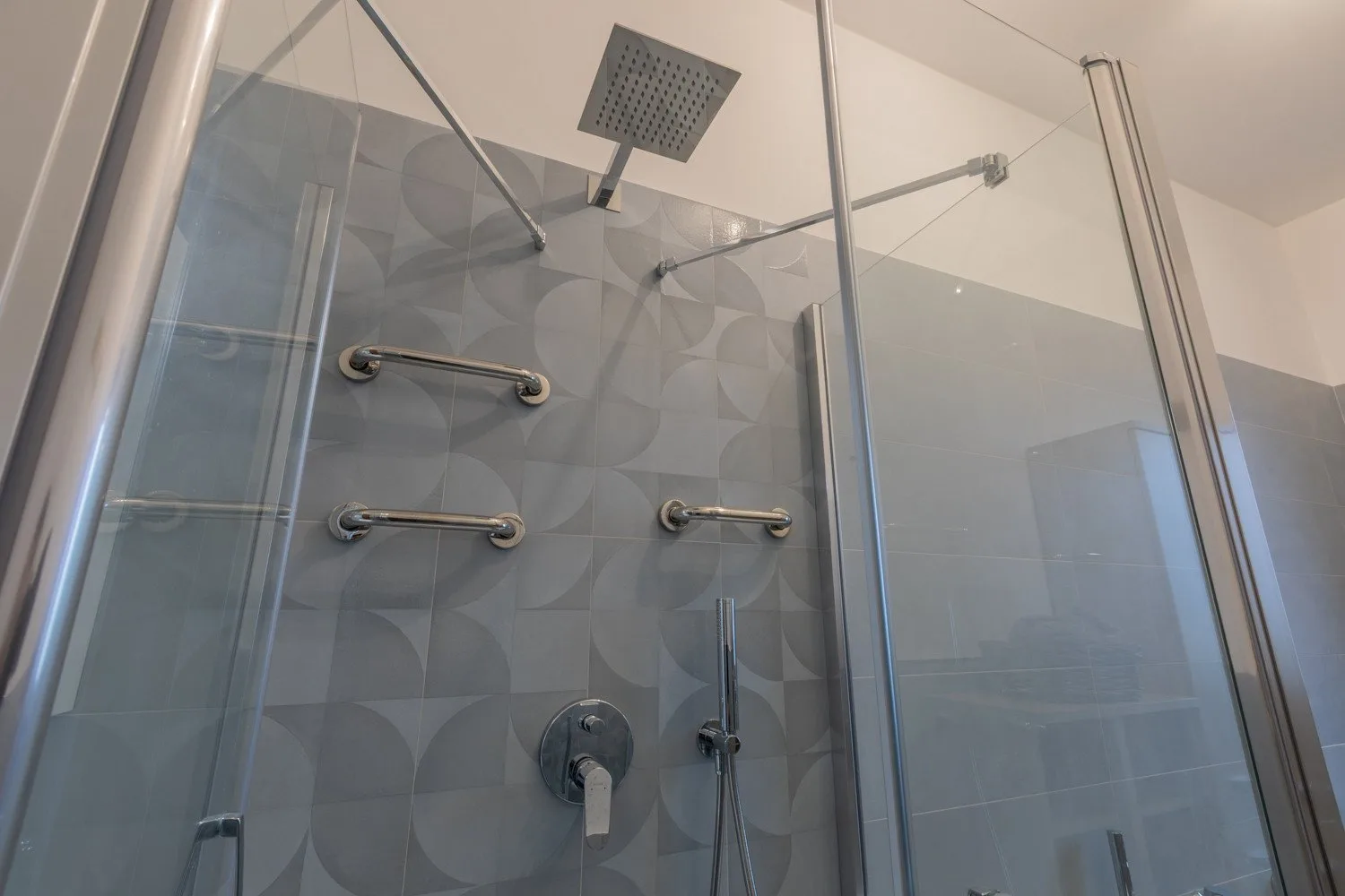 A tiled shower with a square overhead showerhead and wall-mounted controls.