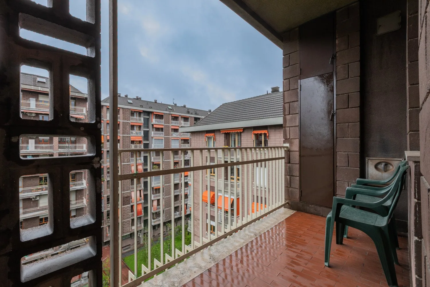 Un balcón cubierto da a un patio de apartamentos, con asientos de plástico junto a la barandilla.