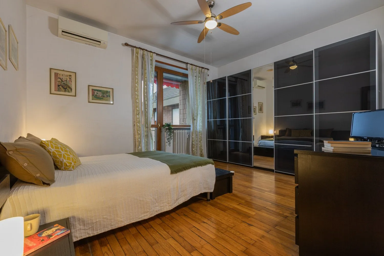 A bedroom with a bed, mirrored wardrobes, and a ceiling fan.