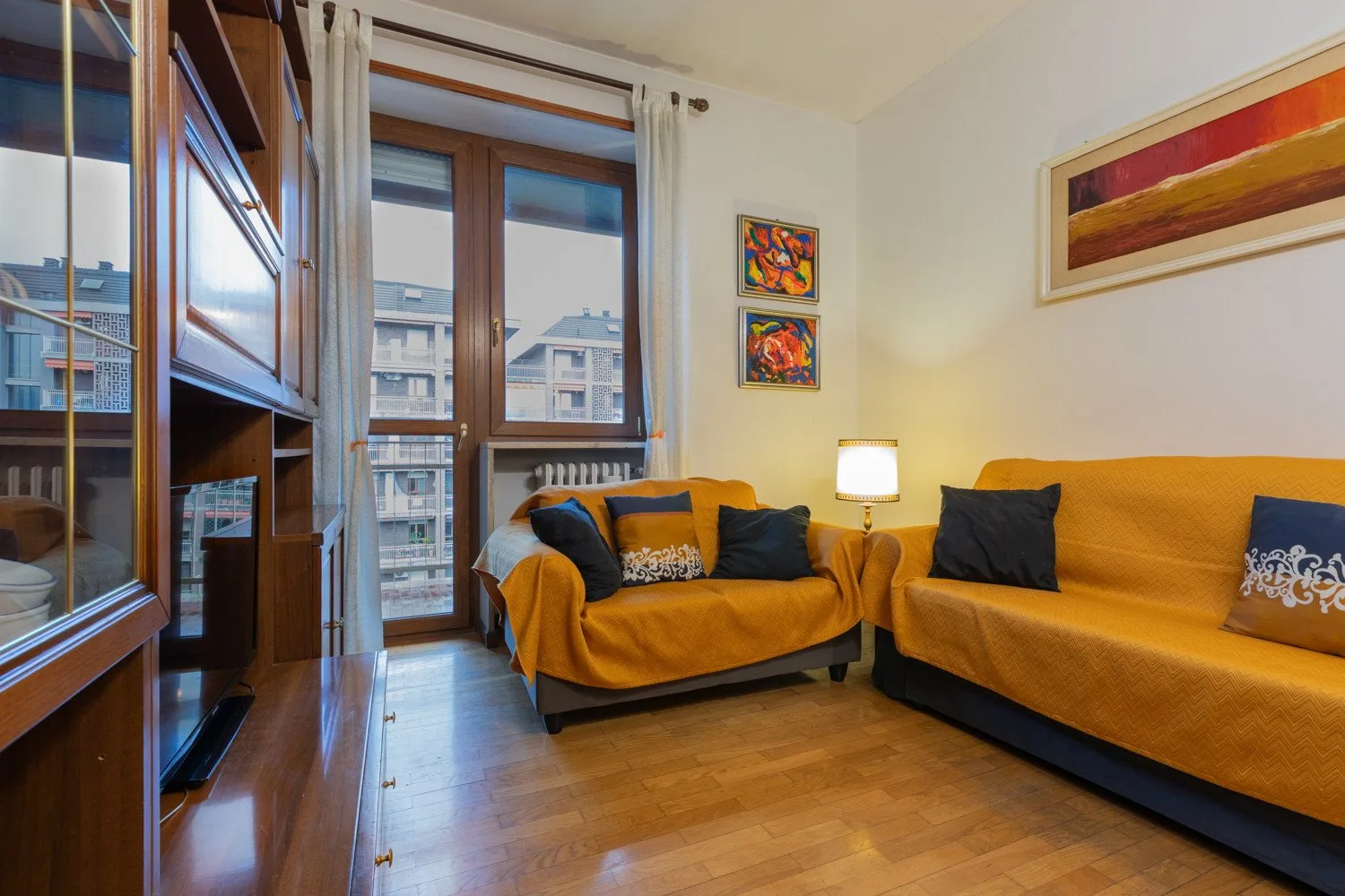 A living room with orange seating, a television cabinet, and tall windows.