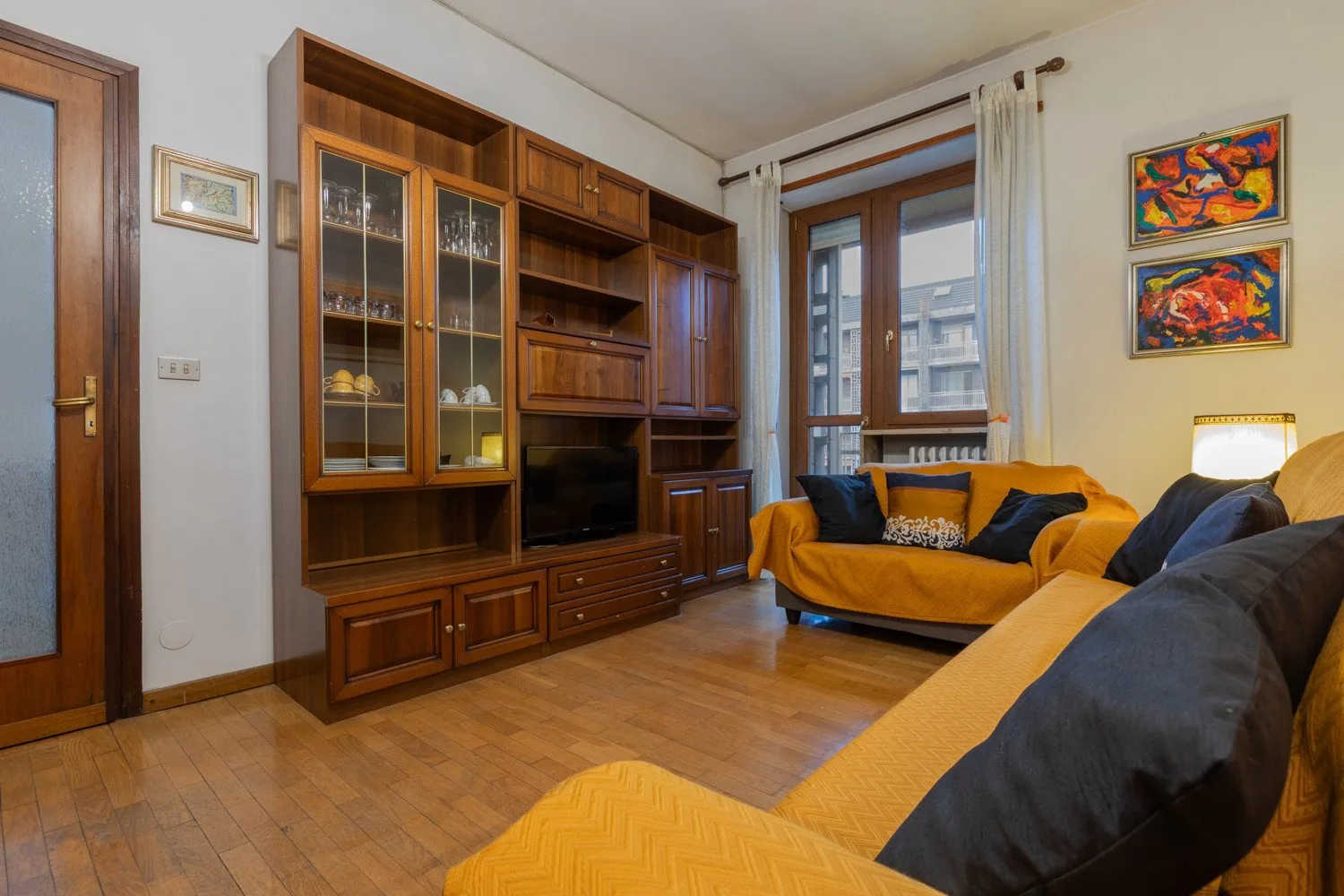 Una sala de estar con asientos de madera, un televisor y una ventana grande.