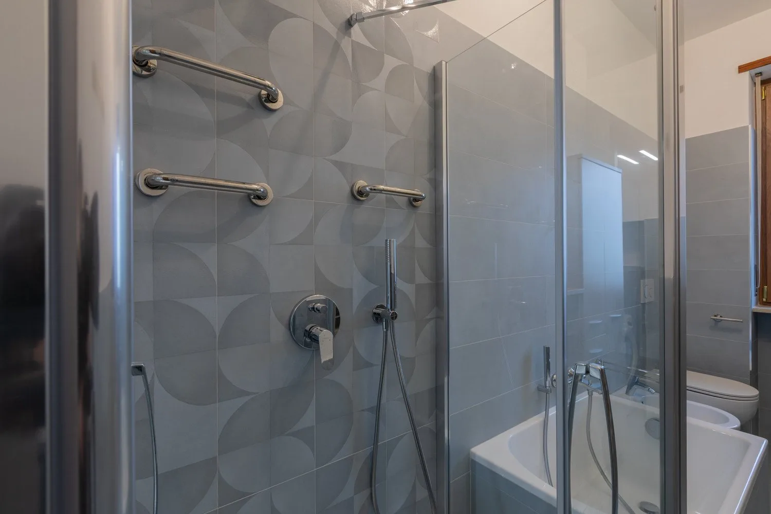 A tiled bathroom with a glass shower enclosure and bathtub.