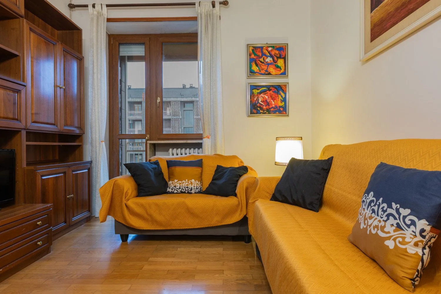A living room with orange seating, a wooden cabinet, and a window with curtains.