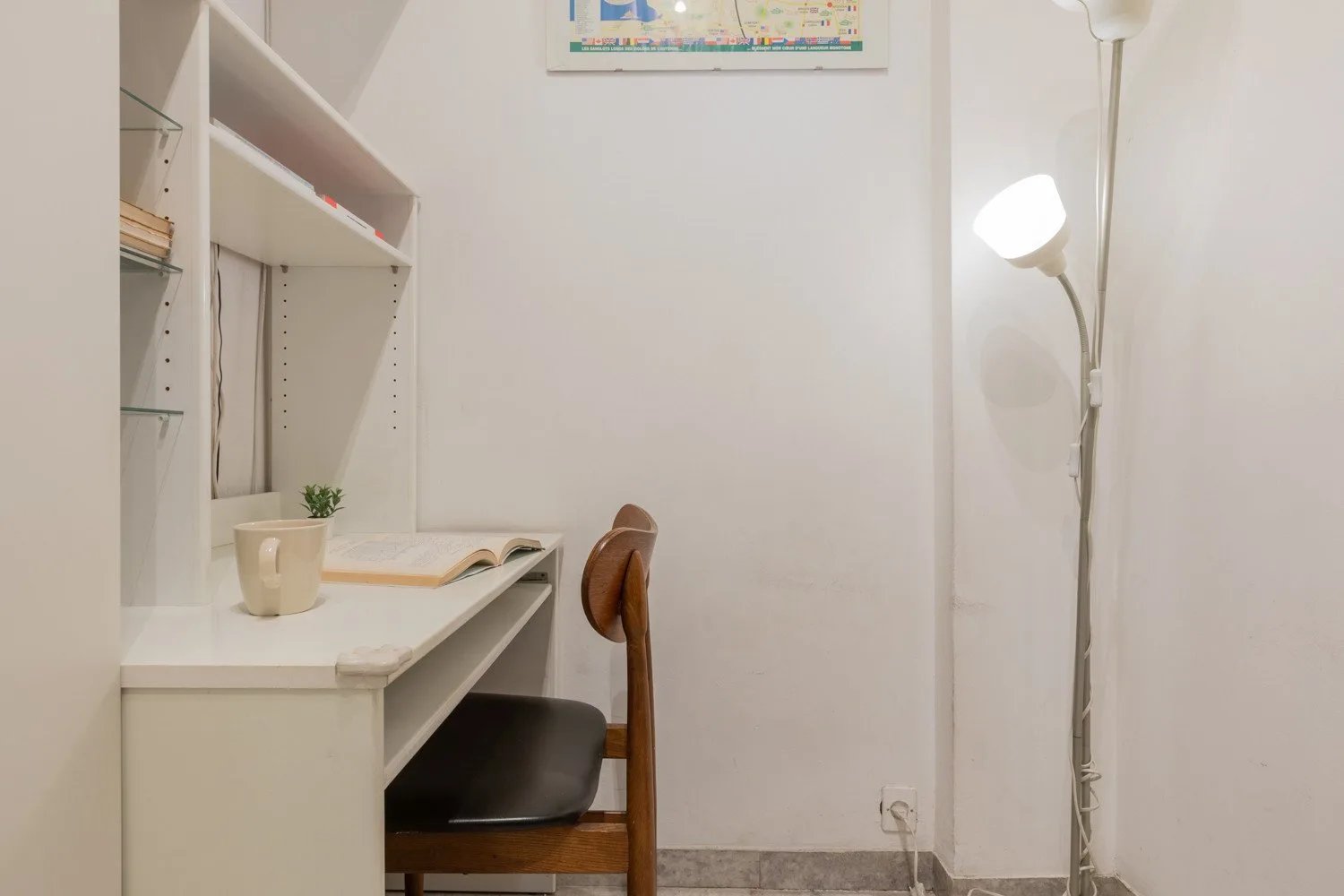 A small study area with a desk, chair, and floor lamp.