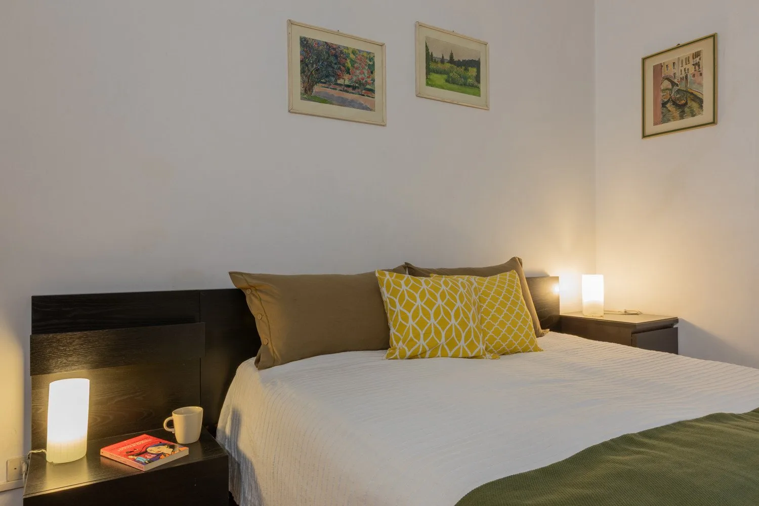 A bedroom with a neatly made bed, patterned cushions, and framed pictures.