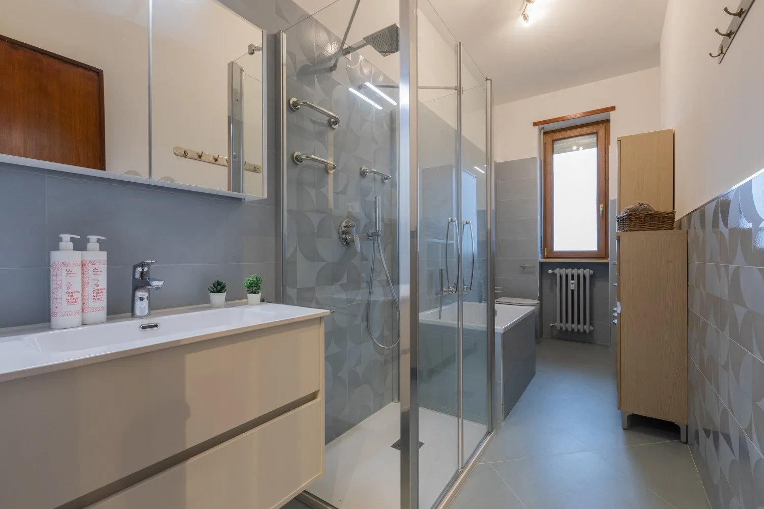 A bathroom with a glass shower, vanity, and window.