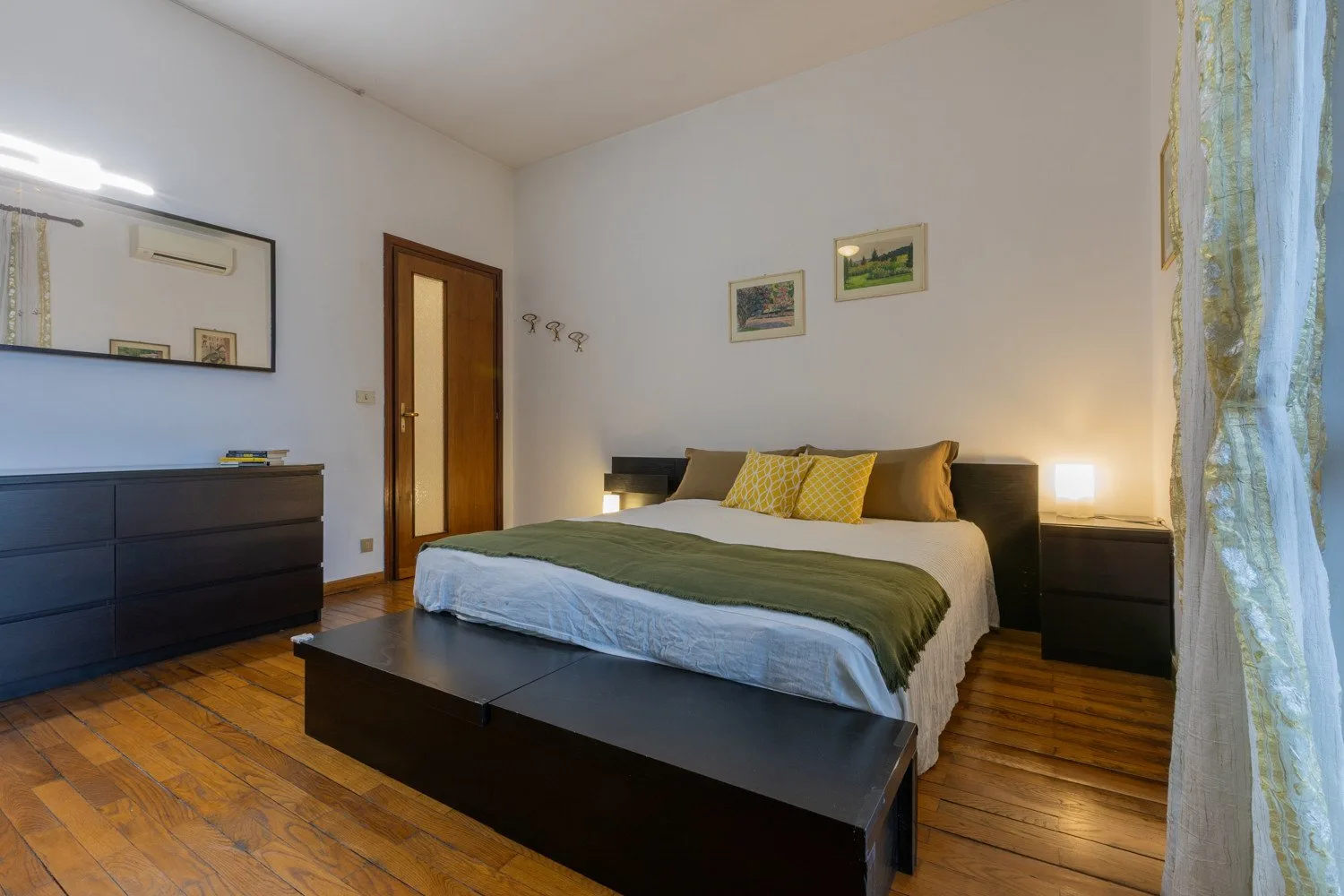 Un dormitorio con una cama tendida, mesitas de noche y suelo de madera.