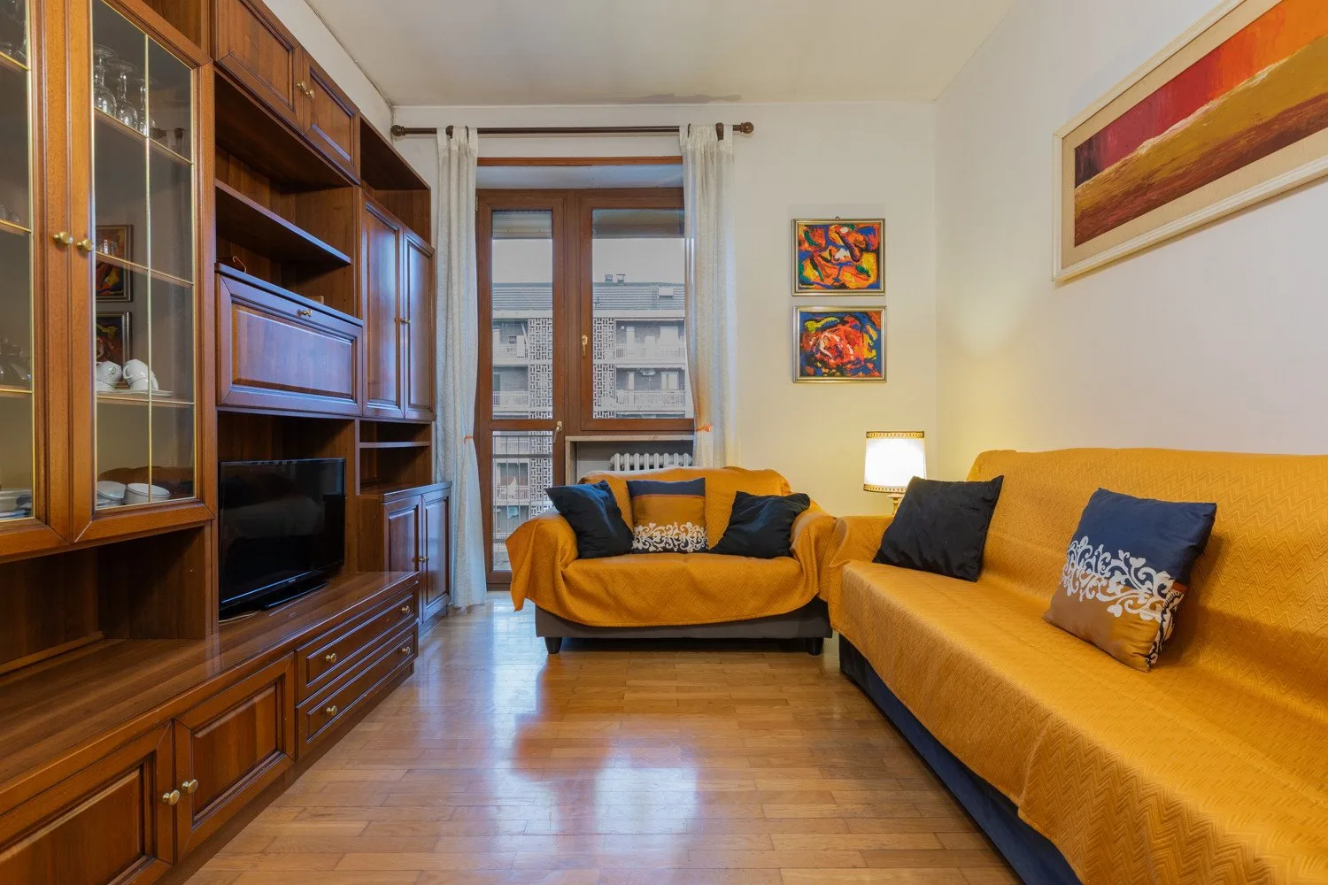 A living room with mustard-colored seating, wooden cabinetry, and a television.