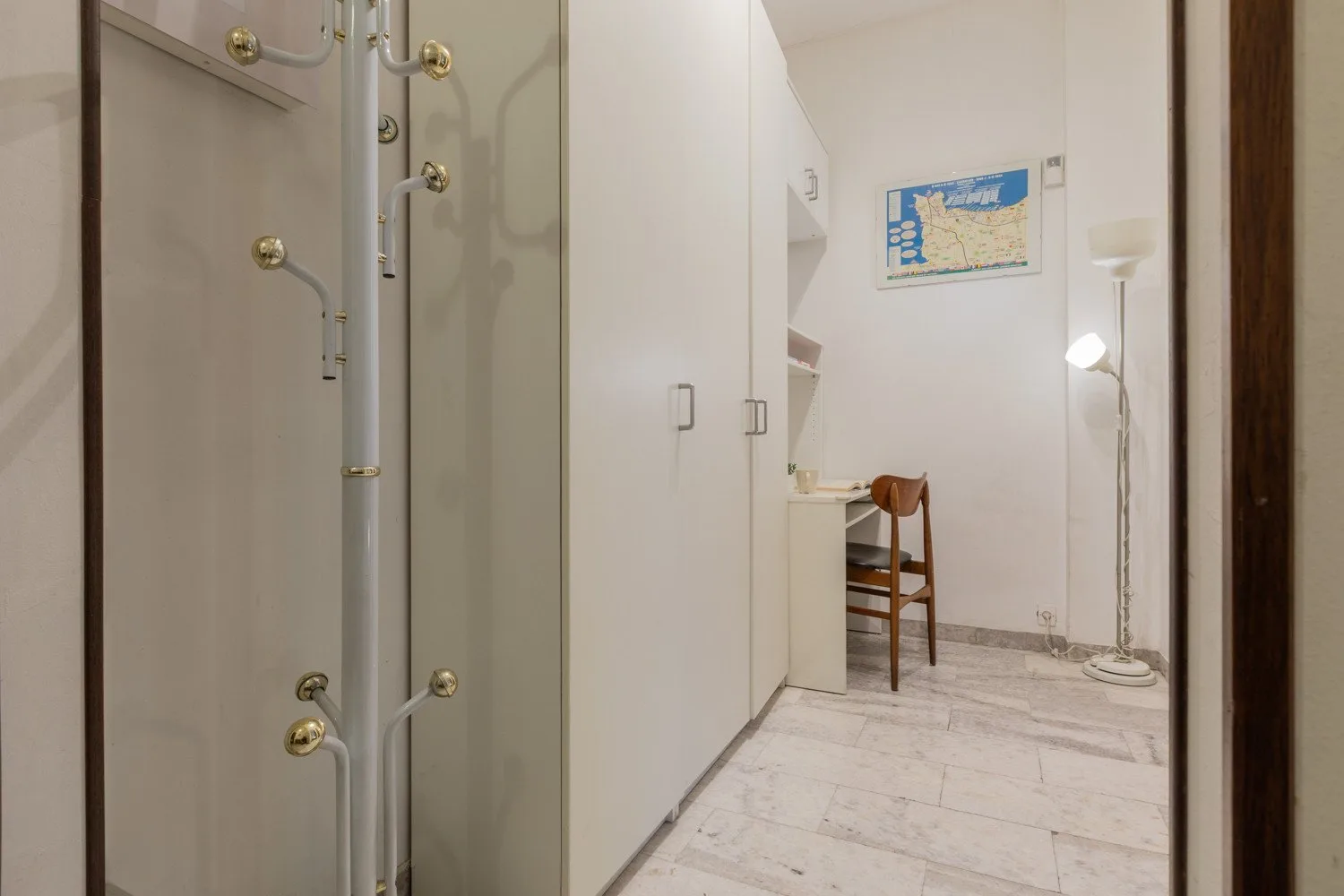 A bright interior hallway with built-in cabinets, a small desk, and a floor lamp.