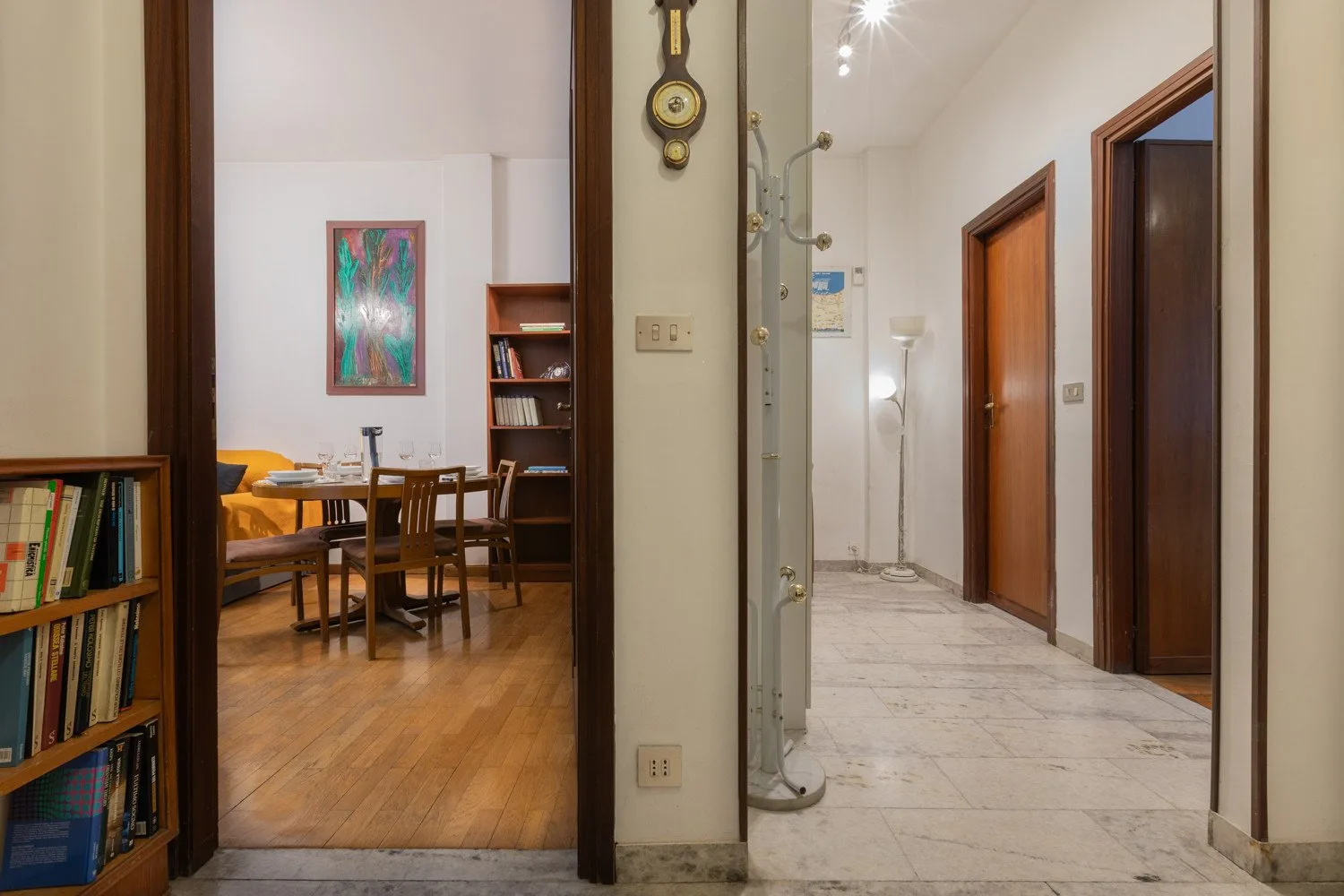 A dining area with a wooden table and chairs opens onto a tiled hallway.