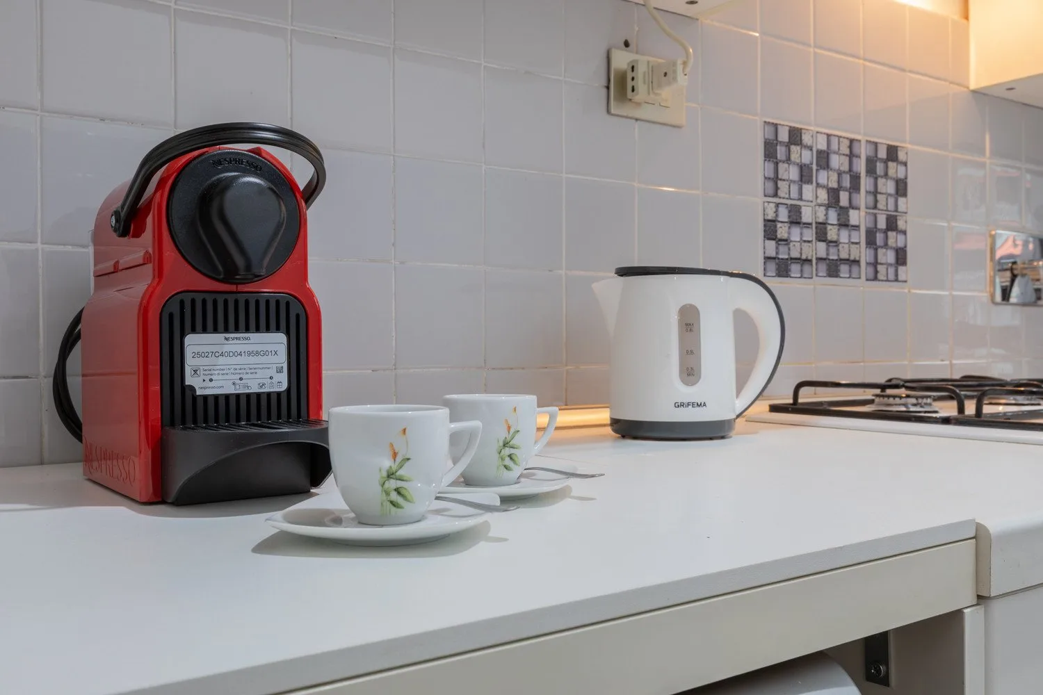 A kitchen counter holds a coffee machine, cups, an electric kettle, and a cooktop.