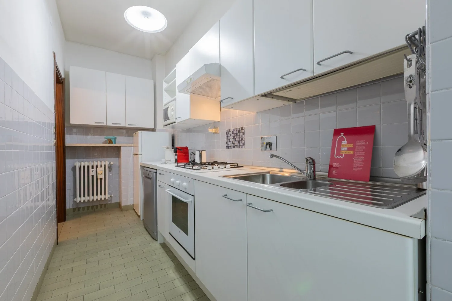 A narrow kitchen with white cabinets, a sink, and a cooktop.
