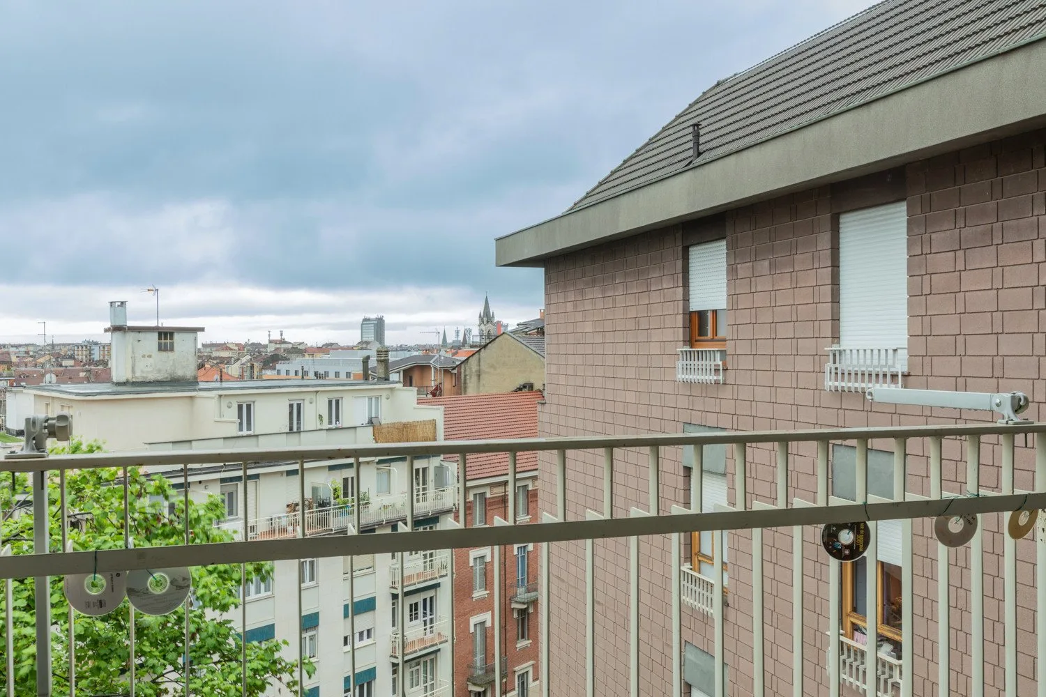 A balcony overlooks nearby apartment buildings beneath a cloudy sky.