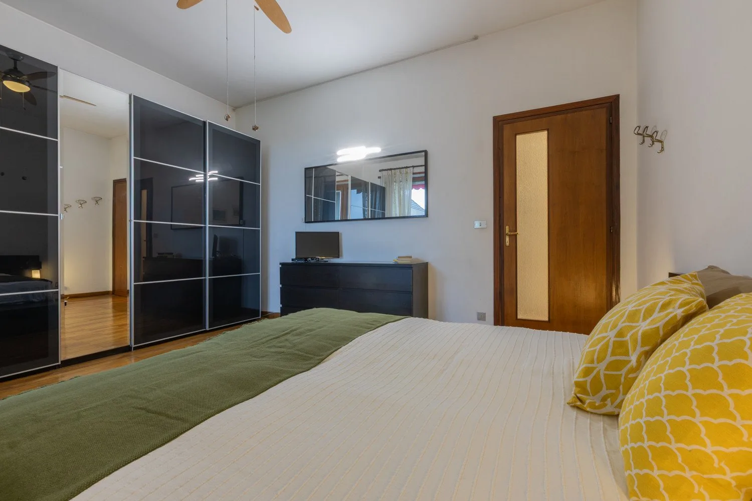 A bedroom with a bed, mirrored wardrobes, and a wooden door.