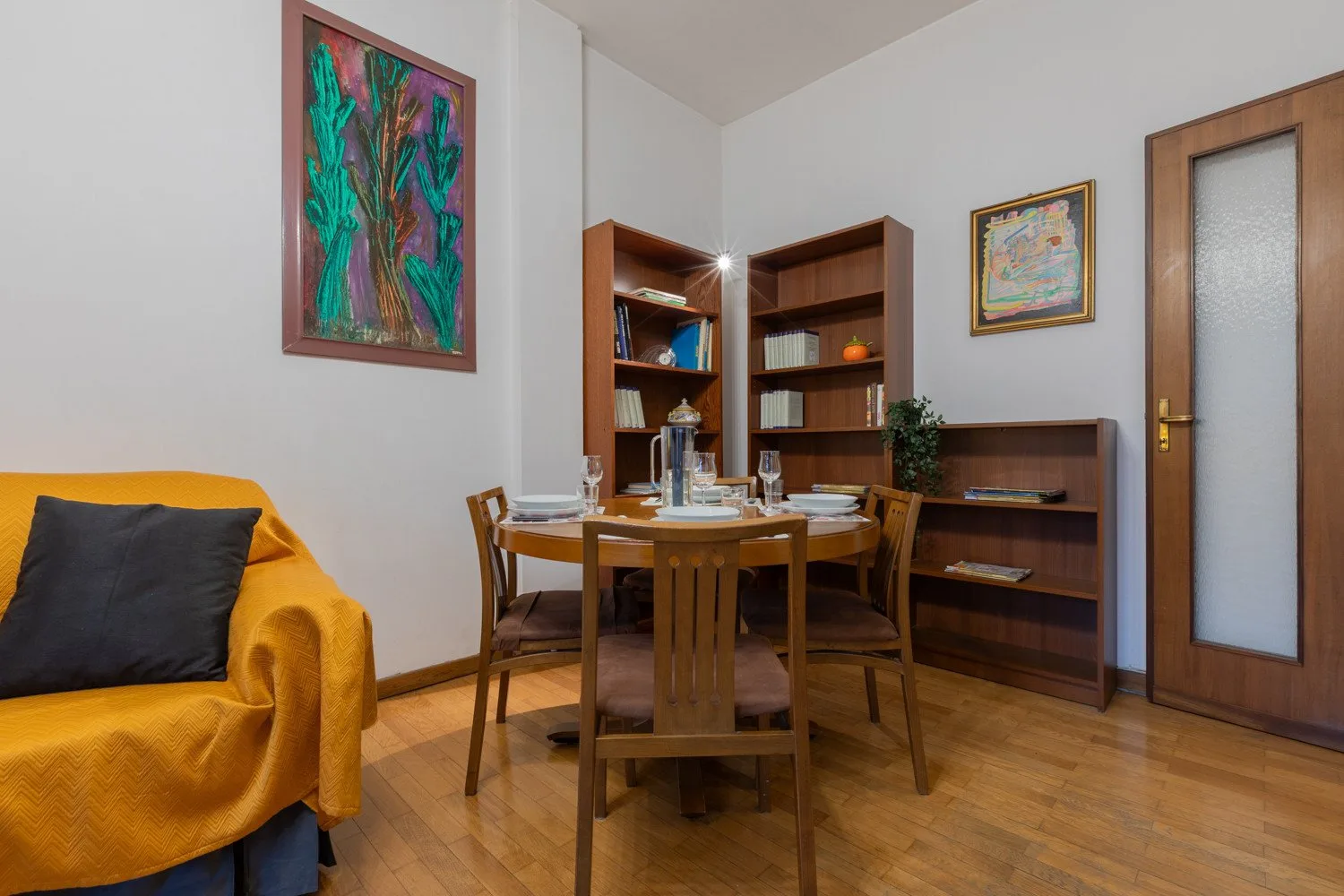A dining area with a wooden table and chairs beside bookshelves.