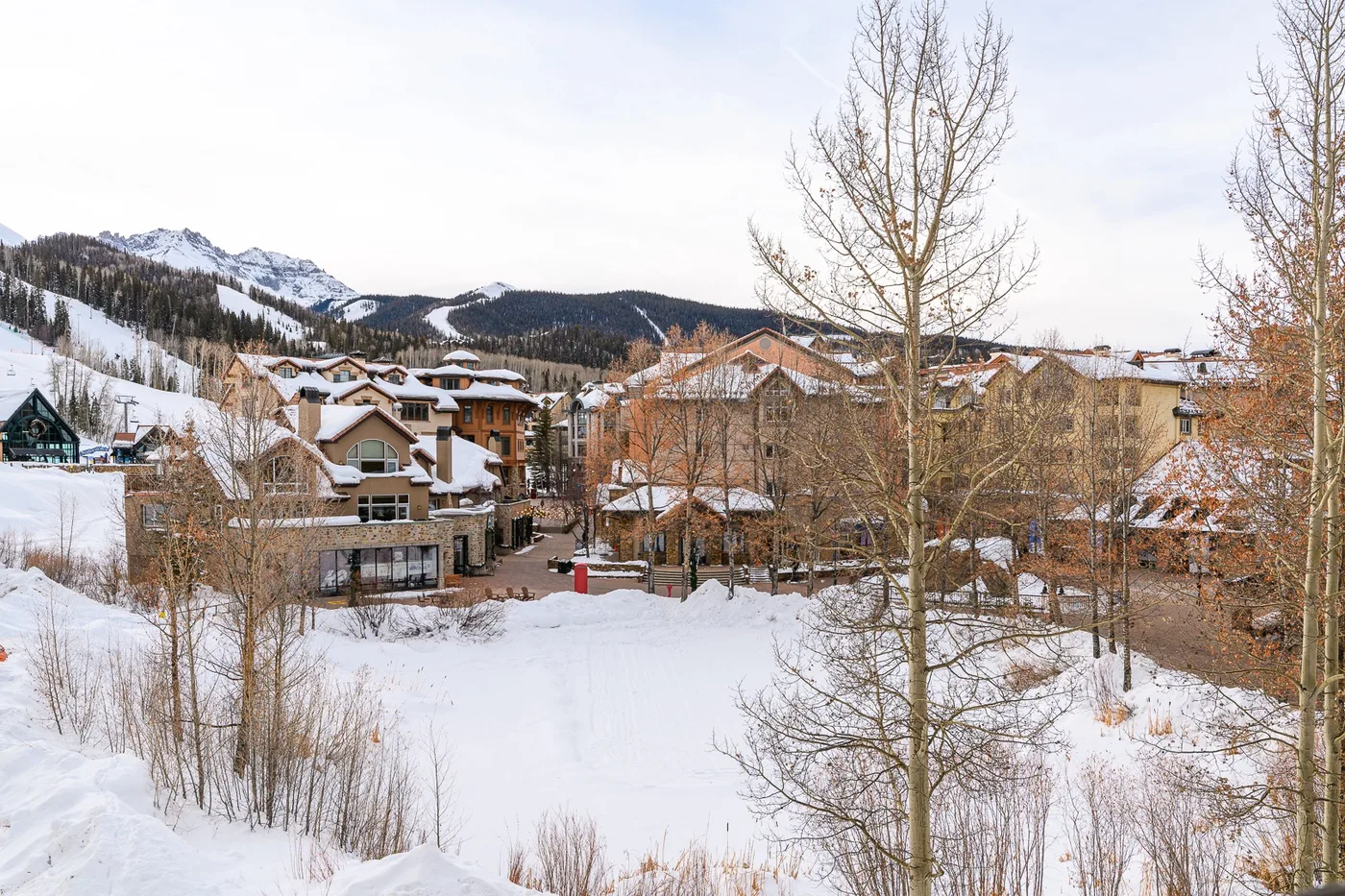 A snow-covered mountain village with clustered buildings and wooded slopes in the background.
