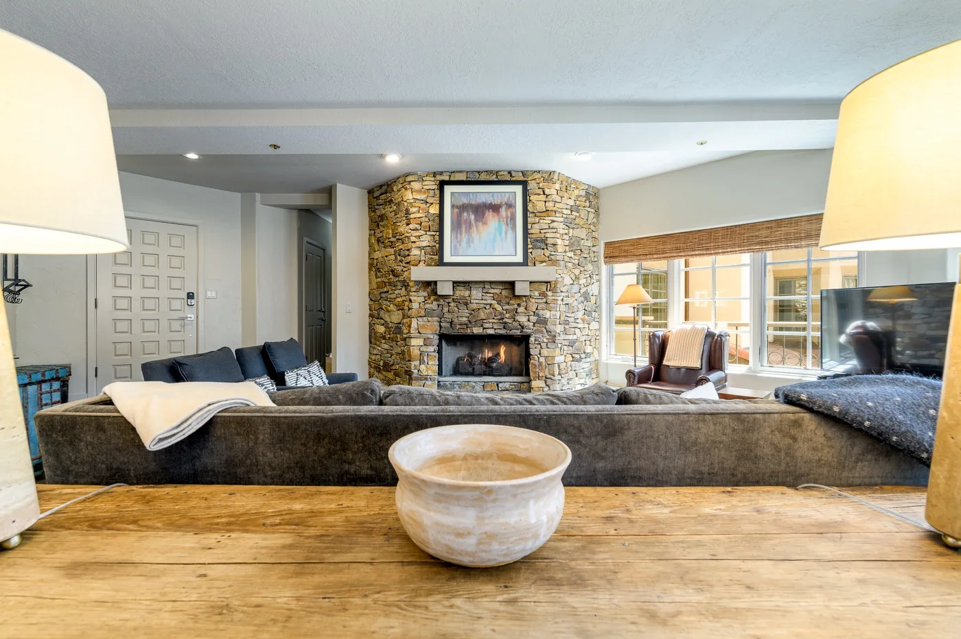 Living room with seating arranged around a stone fireplace and large windows.