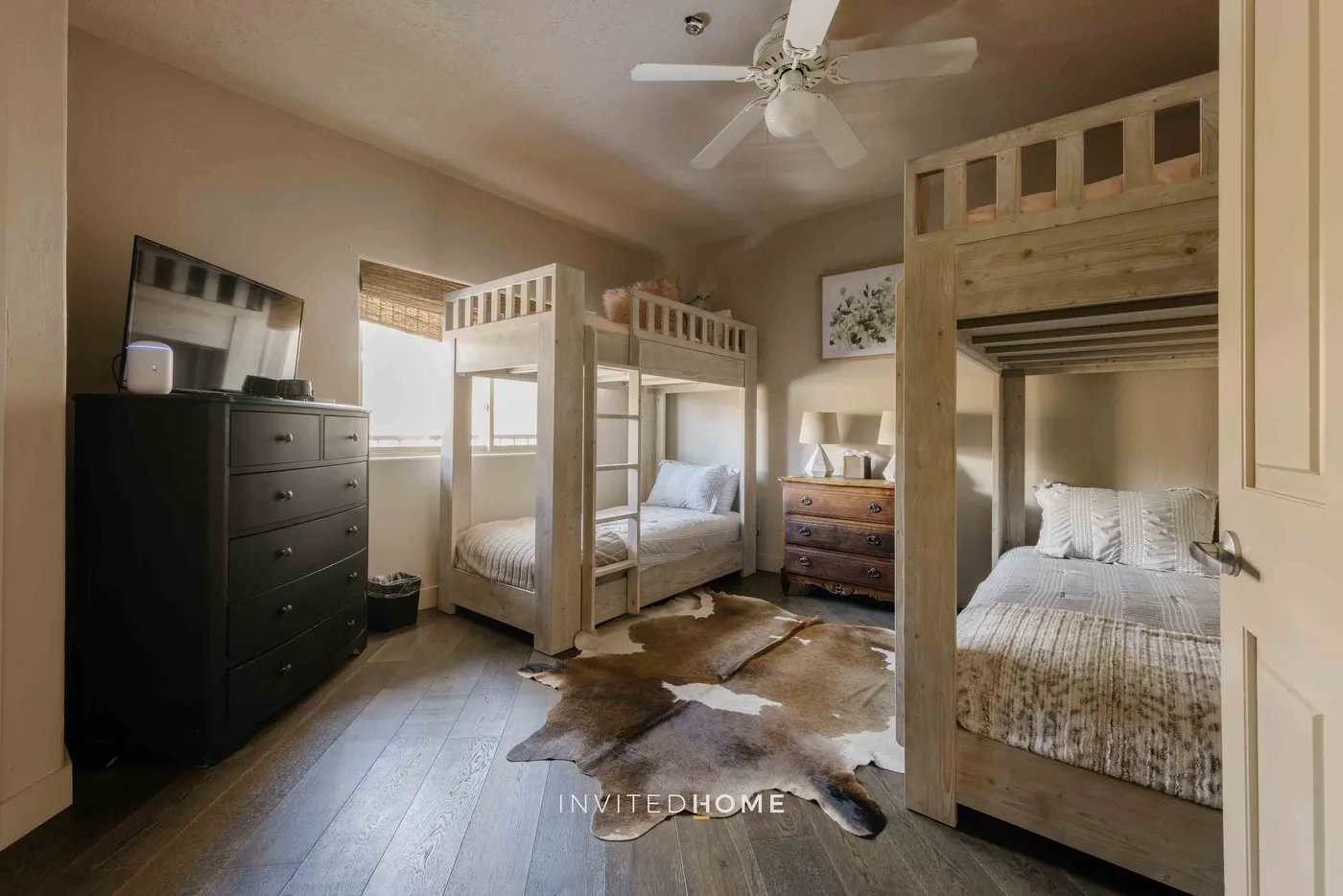 A bedroom with wooden bunk beds, a dresser, and a ceiling fan.