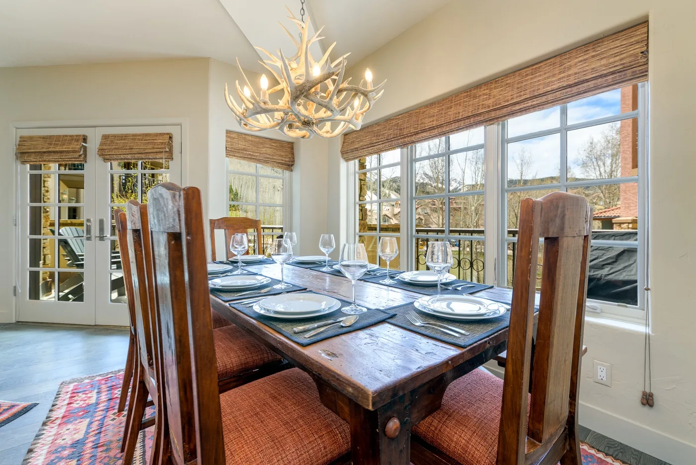 A dining area with a wooden table set beside large windows.