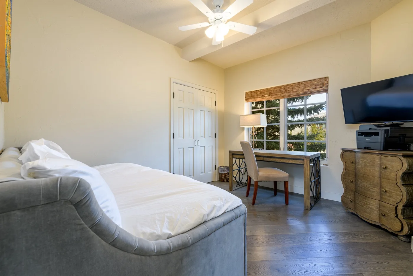 A bedroom with a bed, desk, and window beneath a ceiling fan.