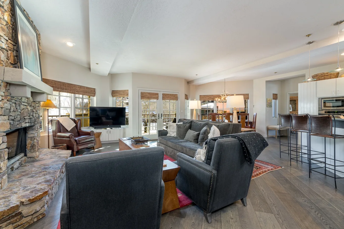 A spacious living room with seating, a stone fireplace, and an open kitchen.