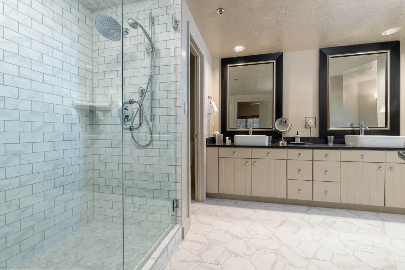 A spacious bathroom with a glass shower and a long vanity beneath two mirrors.