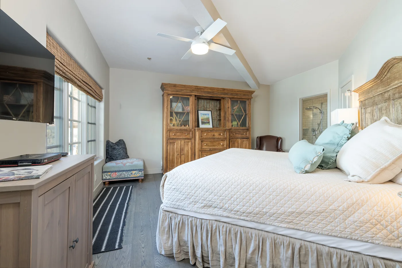 A bright bedroom with a large bed and wooden storage cabinet.