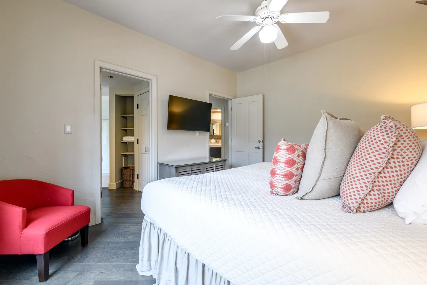 A bedroom with a neatly made bed and a red accent chair.