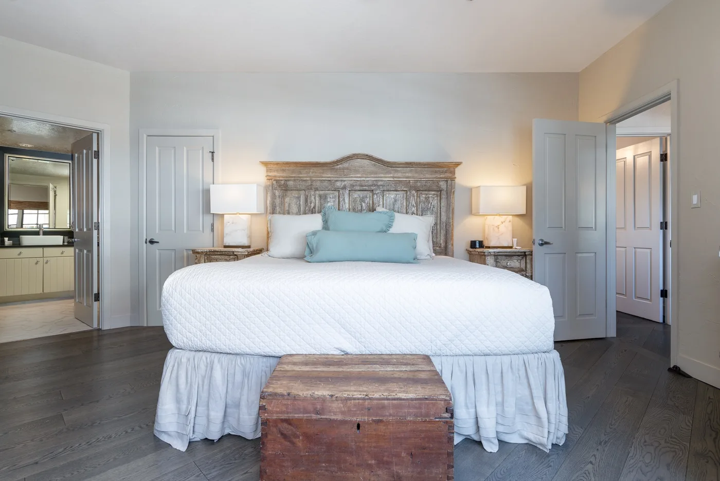 A bedroom with a large bed, bedside lamps, and a wooden chest at the foot.