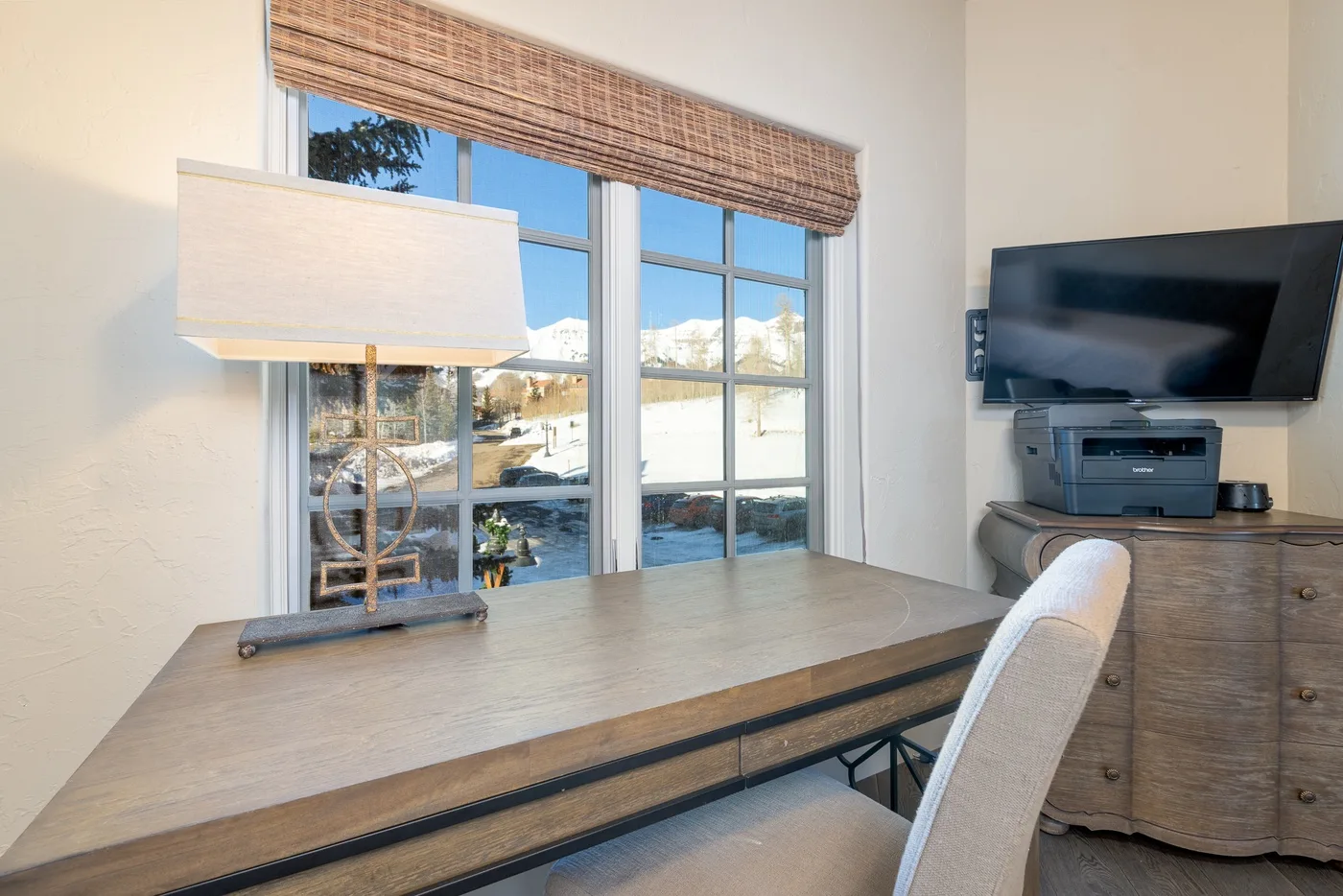 A desk and chair sit beside large windows overlooking a snowy landscape.