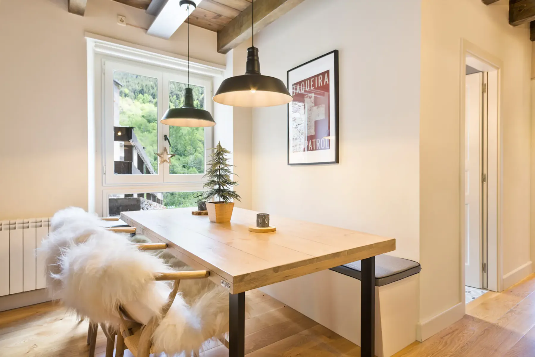 A dining area with a wooden table beneath exposed ceiling beams and pendant lights.