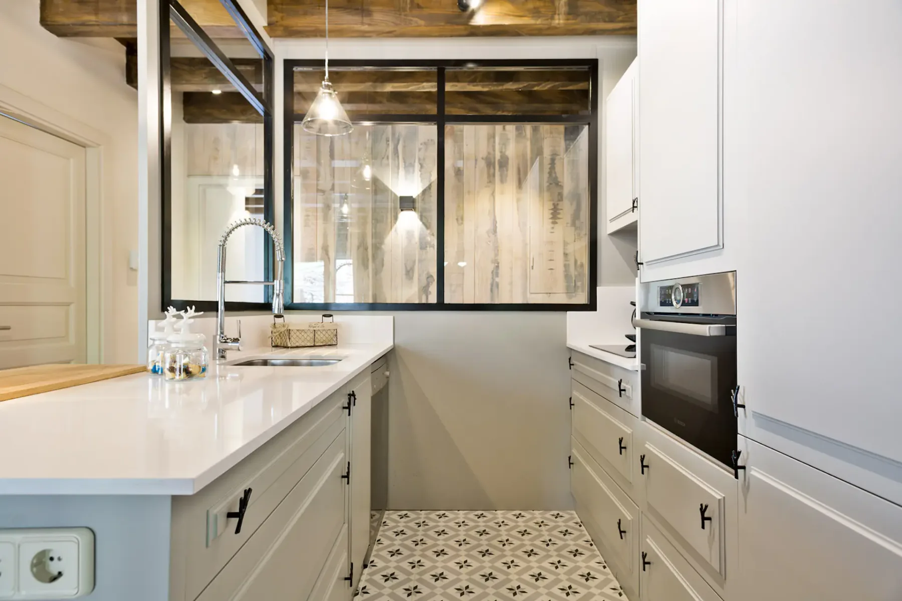 A modern kitchen with white cabinetry, a long counter, and patterned tile flooring.