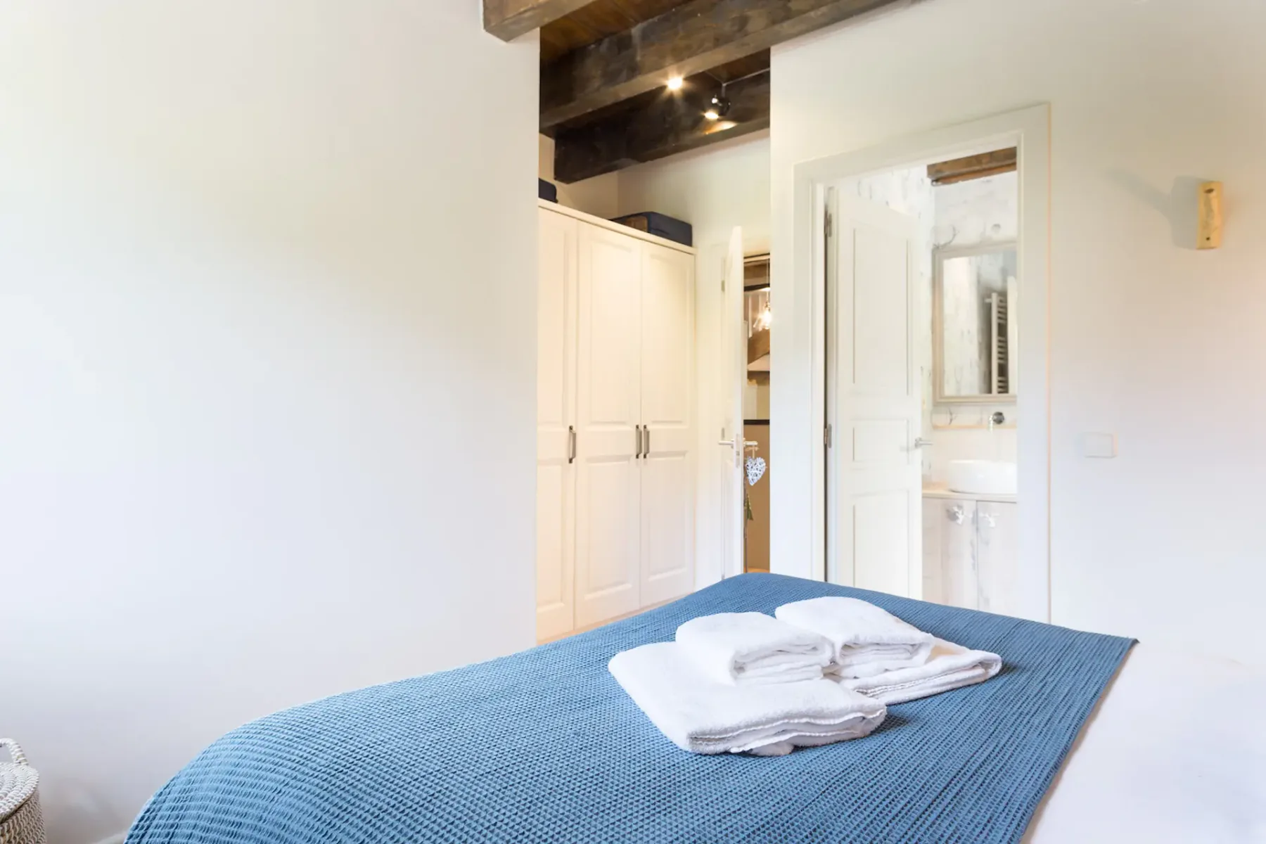 A bedroom with a blue bedspread and folded white towels, with a bathroom visible through the doorway.