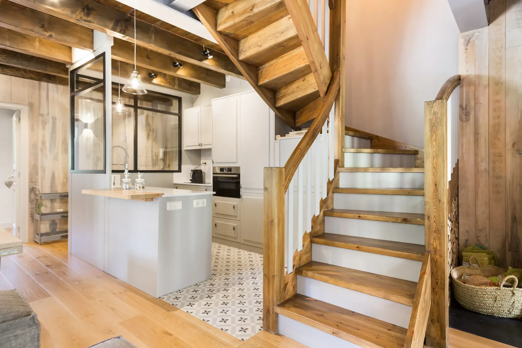 A kitchen with a light island sits beside a wooden staircase.
