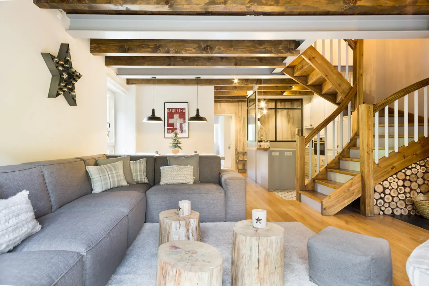 A living room with a gray sectional and wooden coffee tables beneath exposed beams.