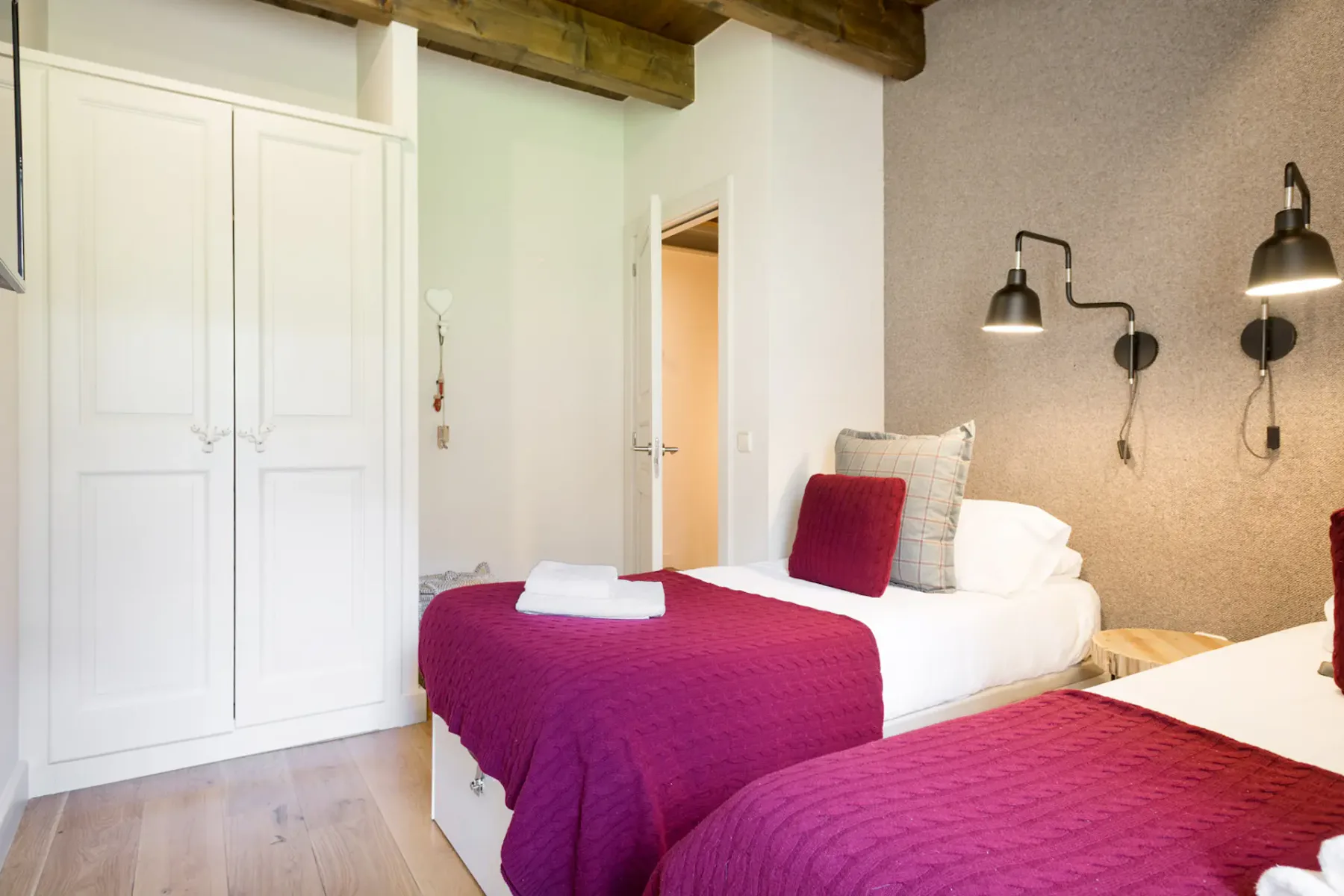 A bedroom with two beds, white wardrobes, and wooden ceiling beams.