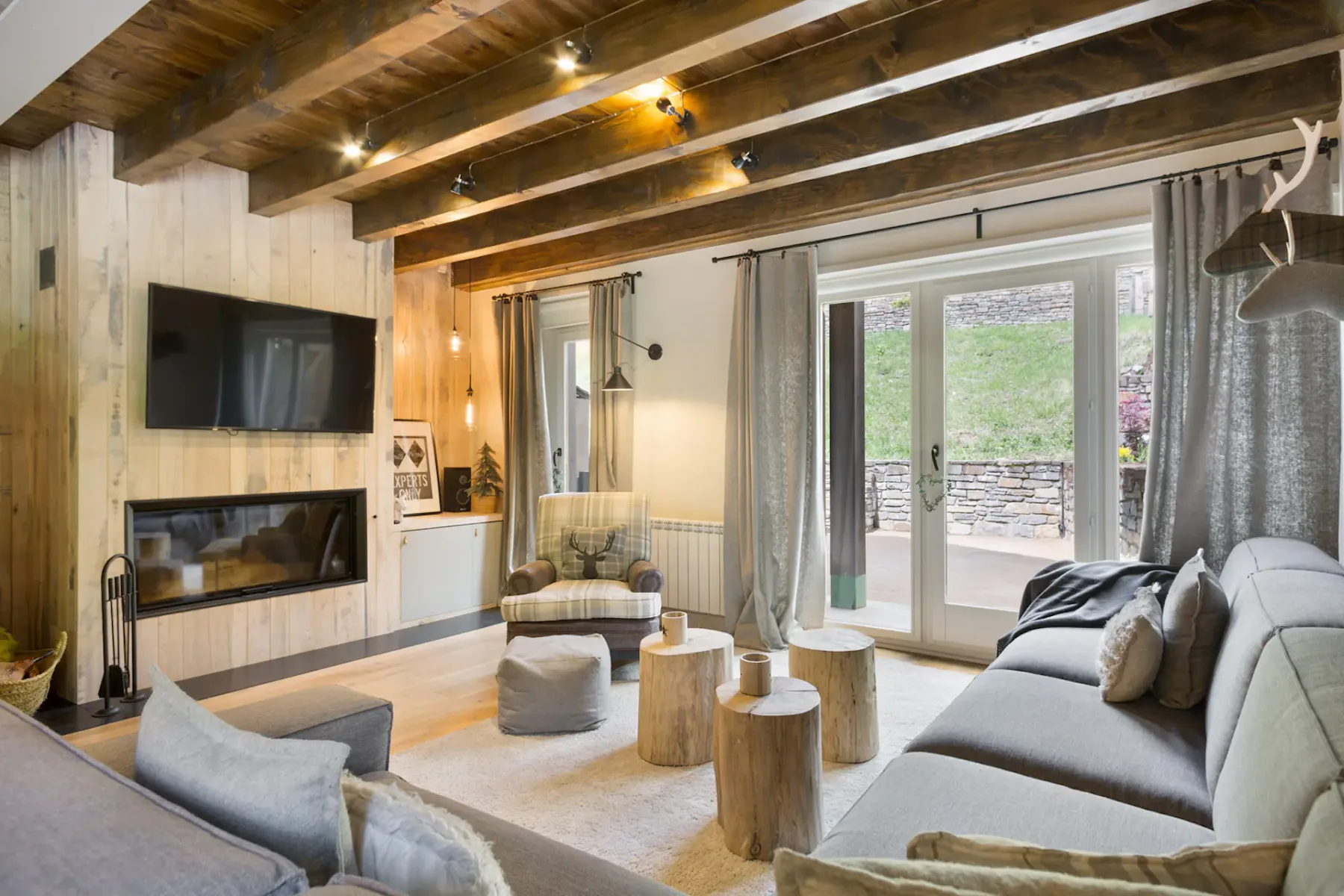 A living room with gray seating, round wooden tables, and large glass doors opening onto a patio.