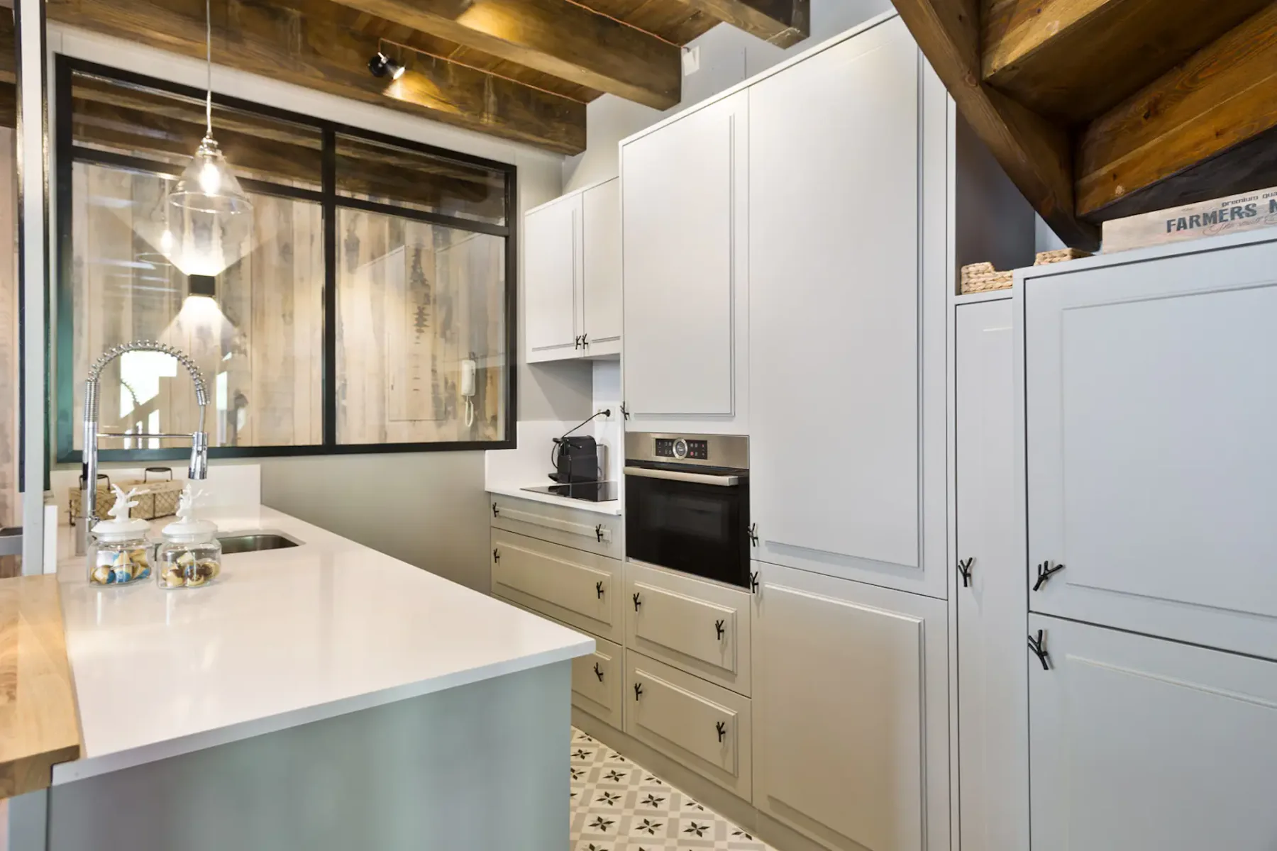 A bright kitchen with white cabinetry, a countertop, and exposed wooden ceiling beams.