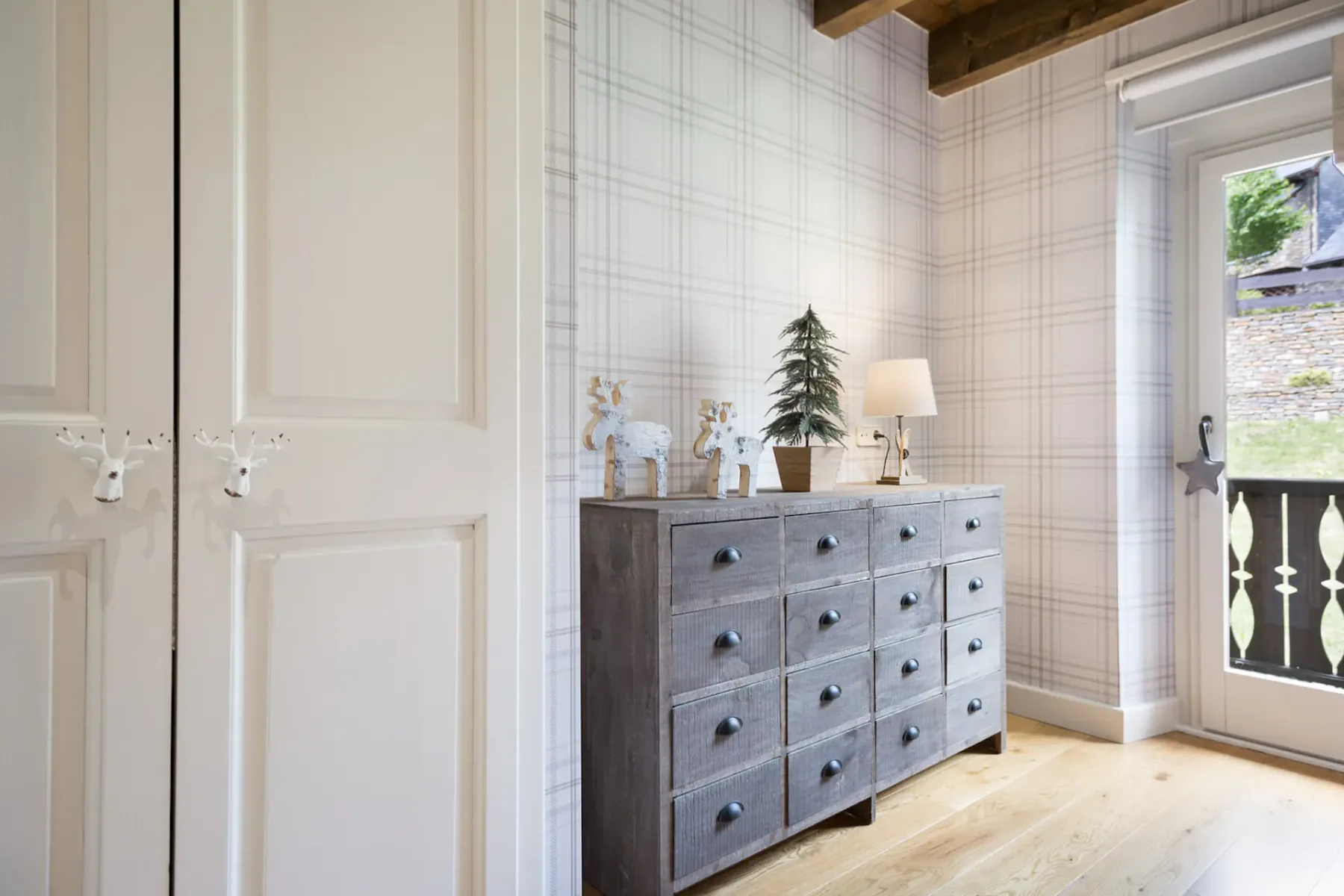 A bedroom with a gray dresser, decorative objects, and a glass door opening to a balcony.