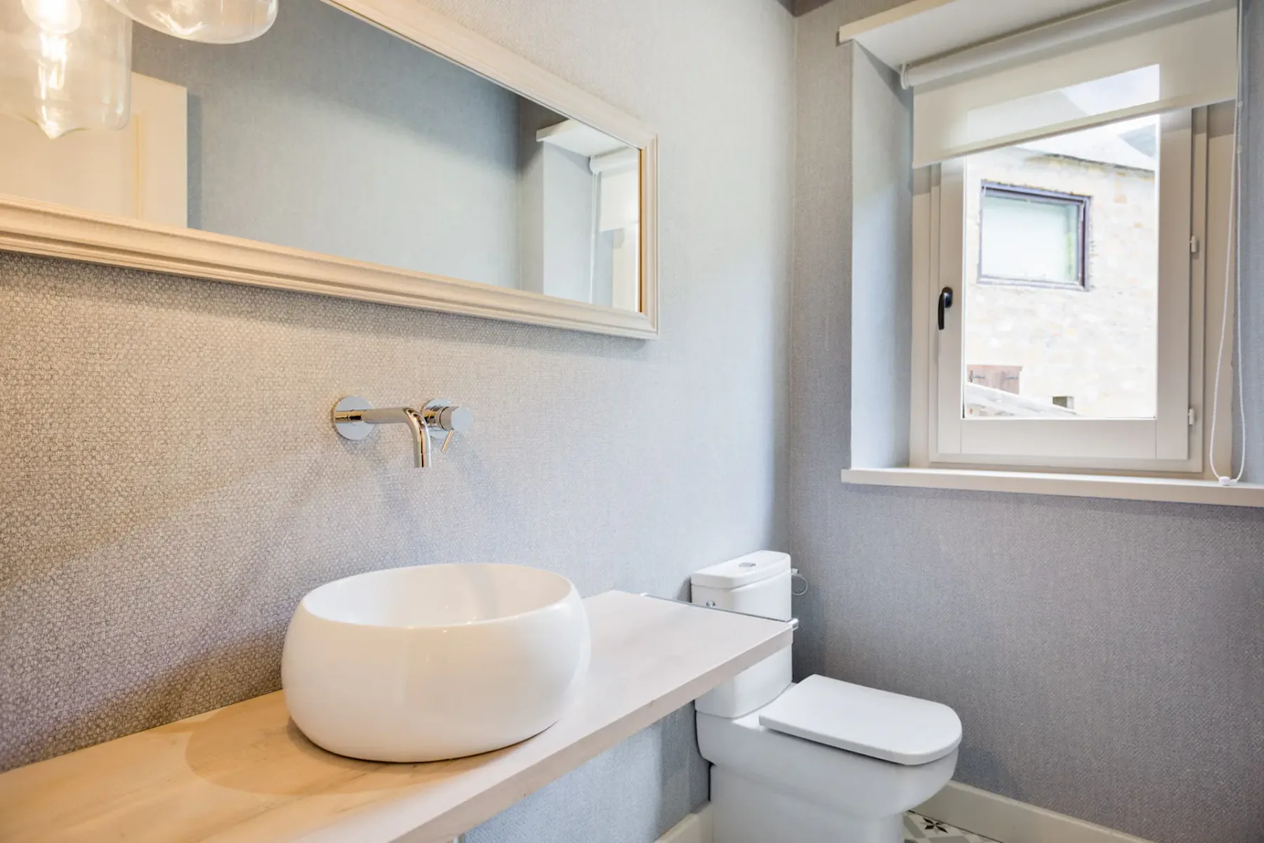 A small bathroom with a vessel sink, toilet, and window.