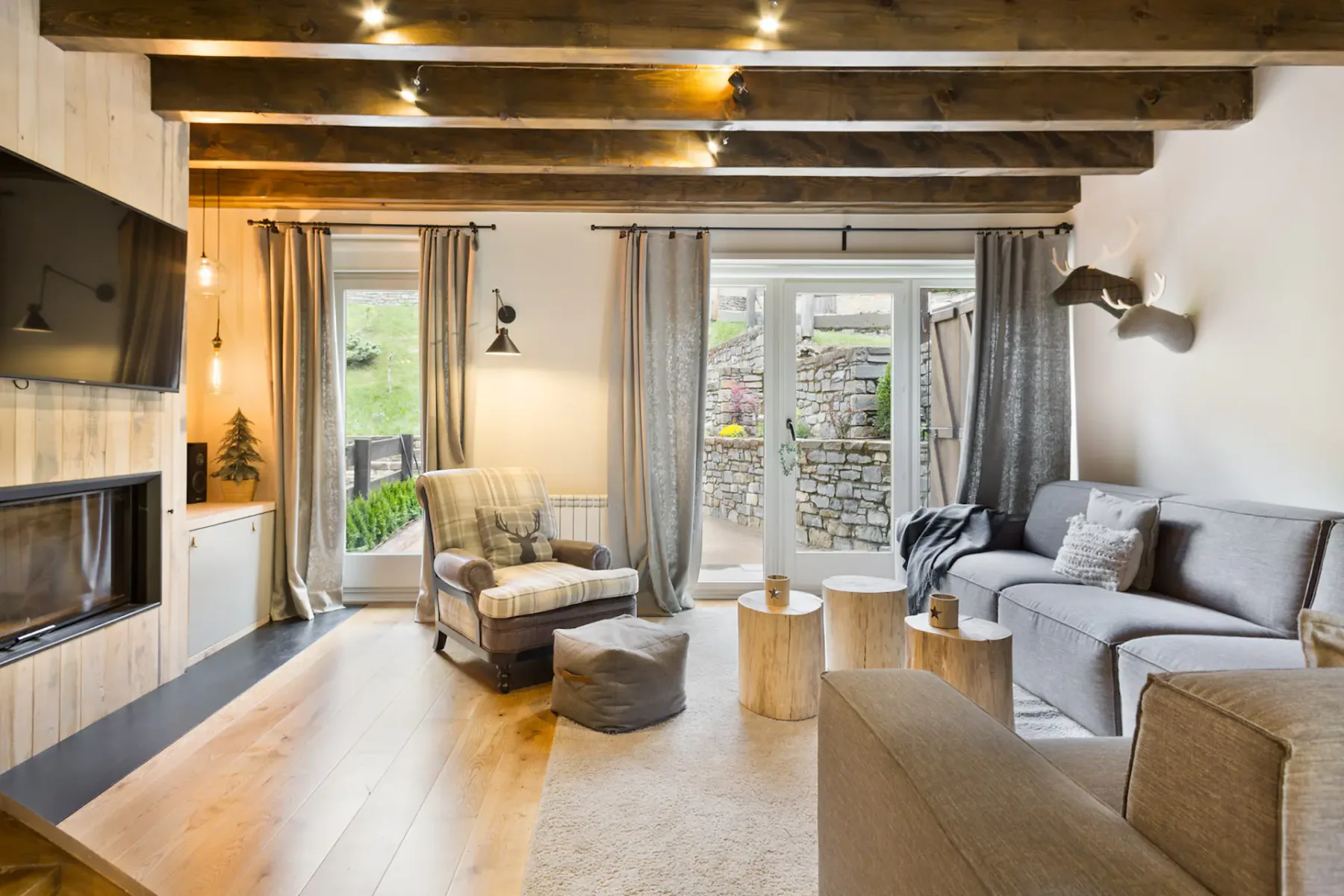 A living room with seating, a coffee table, and large windows opening onto a stone patio.