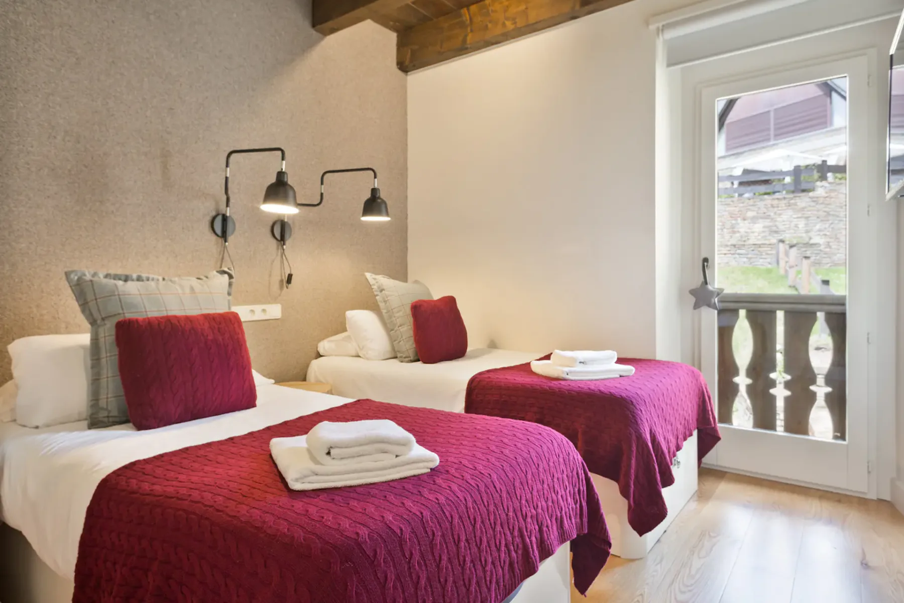 A bedroom with two beds dressed in white and burgundy bedding beside a glass door.
