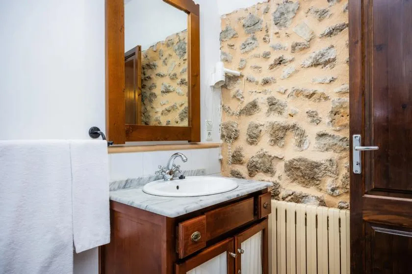 A bathroom vanity with a mirror stands beside a stone wall and radiator.