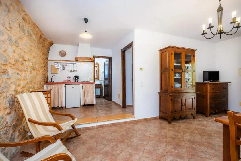 A living area with a compact kitchen, wooden cabinet, and cushioned seating.