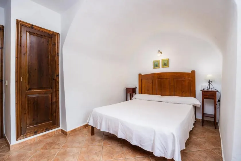 A bedroom with a wooden bed frame, white bedding, and a wooden door.
