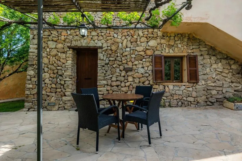 A stone courtyard with a shaded table and seating beside a stone building.
