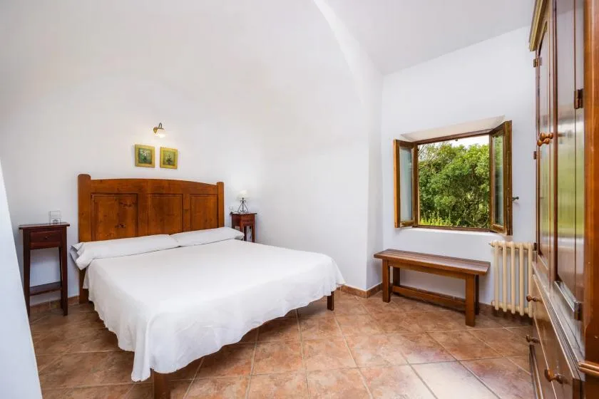 A bedroom with a wooden bed, white bedding, and a window overlooking greenery.