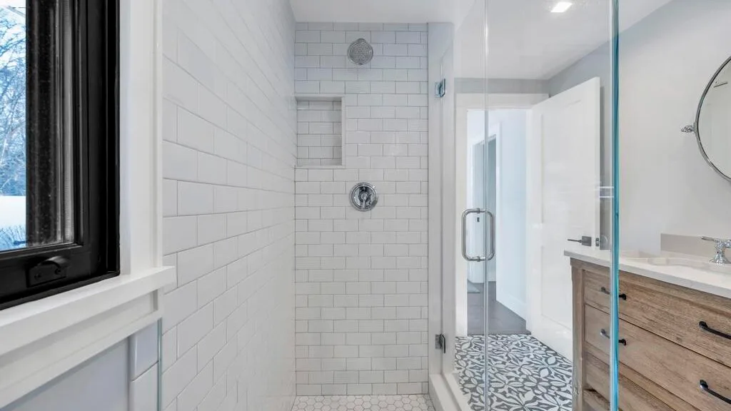 Un baño alicatado con ducha de vidrio, tocador de madera y suelo estampado.